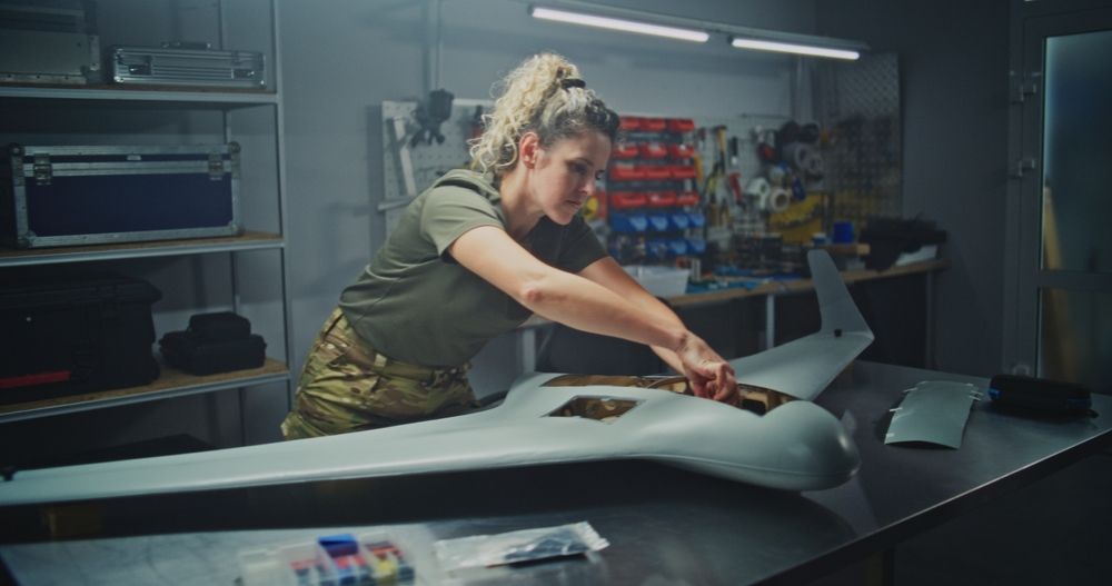 Adult Woman Engineer in Military Uniform Meticulously Assembles Large UAV Alongside Male Colleagues. Concept of Gender Diversity and Professional Expertise in Defense Engineering and Refining UAV