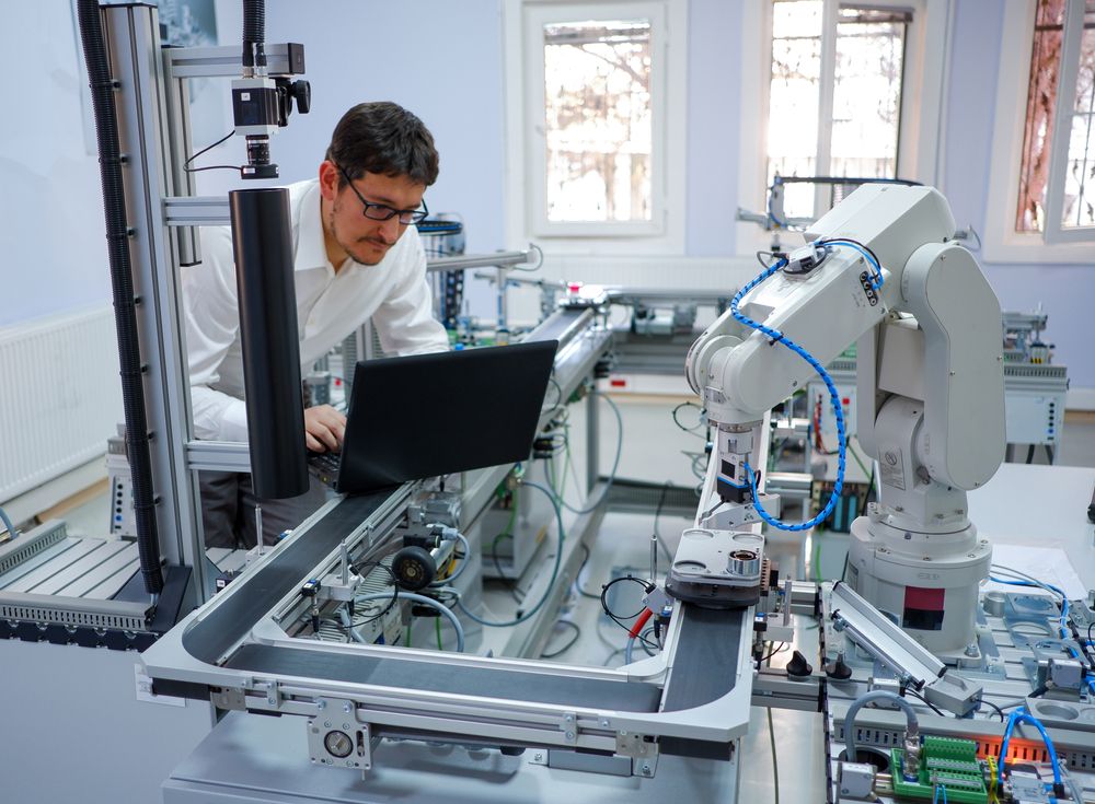 Close-up robot arm. Engineer is working on laptop to programming smart factory automation and automated car on production line