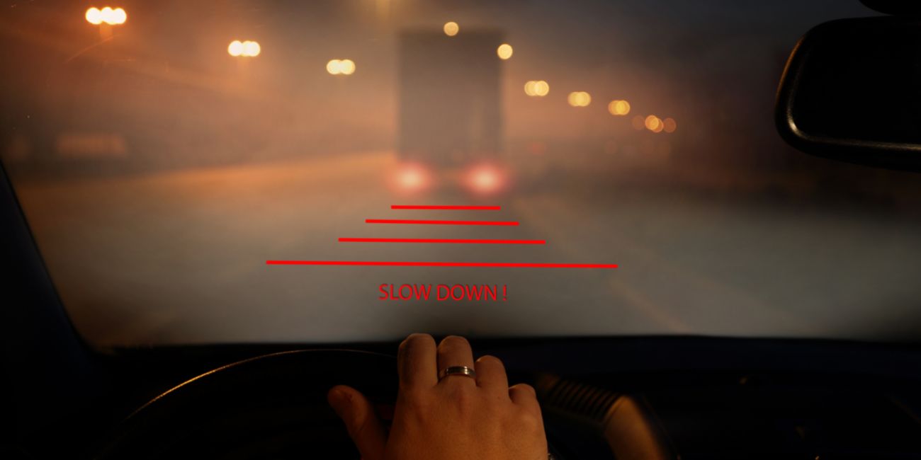 A driver's point-of-view through a foggy windshield at night with an augmented reality heads-up display showing a 'Slow Down' warning, illustrating an ADAS safety application that depends on high-fidelity sensor and camera signal chains.