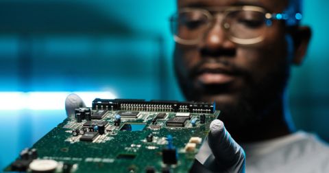 Engineer examining a printed circuit board under blue lighting.
