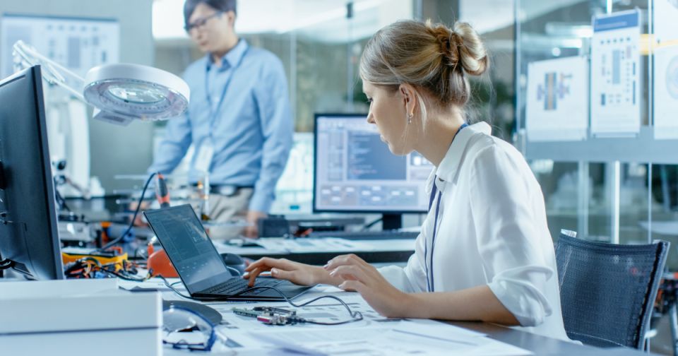 Une informaticienne connecte une carte de circuit imprimé à son ordinateur portable avec un écran vert factice. Elle travaille dans un laboratoire technologiquement avancé.